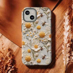 Pu&ograve; includere: Custodia per telefono bianca con un design floreale 3D con margherite bianche e centri gialli. Api sparse in tutto il design.