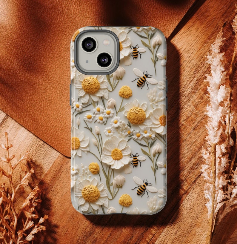 Pu&ograve; includere: Custodia per telefono bianca con un design floreale 3D con margherite bianche e centri gialli. Api sparse in tutto il design.