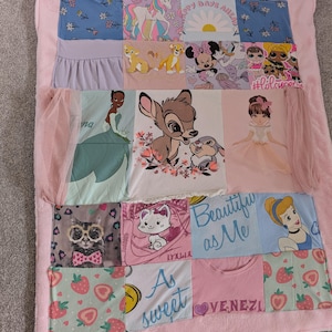 May include: A patchwork quilt featuring various fabric squares with cartoon characters, including a unicorn, Simba, Minnie Mouse, Bambi, Thumper, Marie, and Cinderella. The quilt has a soft pink plush border and includes text such as Happy Days Ahead, #lolsurprise, Beautiful as Me, As sweet, and VENEZIA.