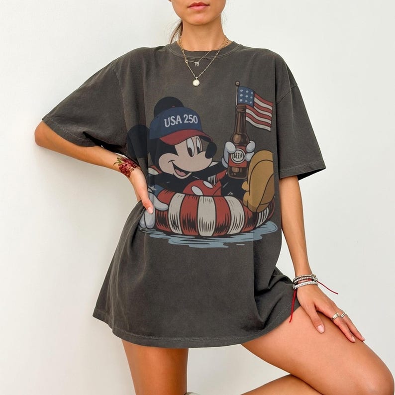 Cartoon pig in a hat with "USA 250" holding a beer and flag on a t-shirt.