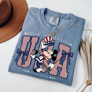 Mickey Mouse in patriotic attire with "USA" and "250th Anniversary 1776–2026" on a blue t-shirt.