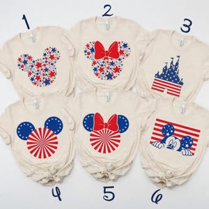 1. Red, white, and blue stars in a Mickey silhouette on a t-shirt. 2. Minnie silhouette with red bow and star pattern on a t-shirt. 3. Castle with American flag design in red, white, and blue on a t-shirt. 4. Mickey silhouette with starry ears and re