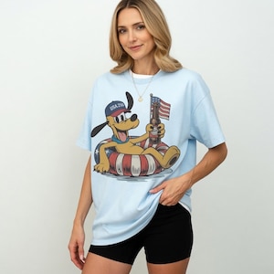 Donald Duck in patriotic attire with "USA 250" text holding a flag on a t-shirt.
