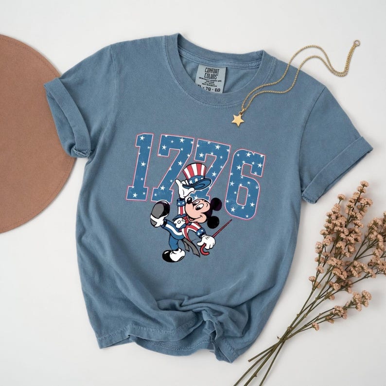 Mickey Mouse in patriotic attire with "1776" and stars on a blue t-shirt.