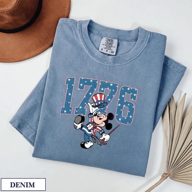 Mickey Mouse in patriotic attire with "1776" in star-patterned letters on a denim t-shirt.