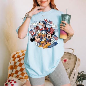 Mickey and Friends in patriotic hats with American flags and fireworks on a light blue t-shirt.