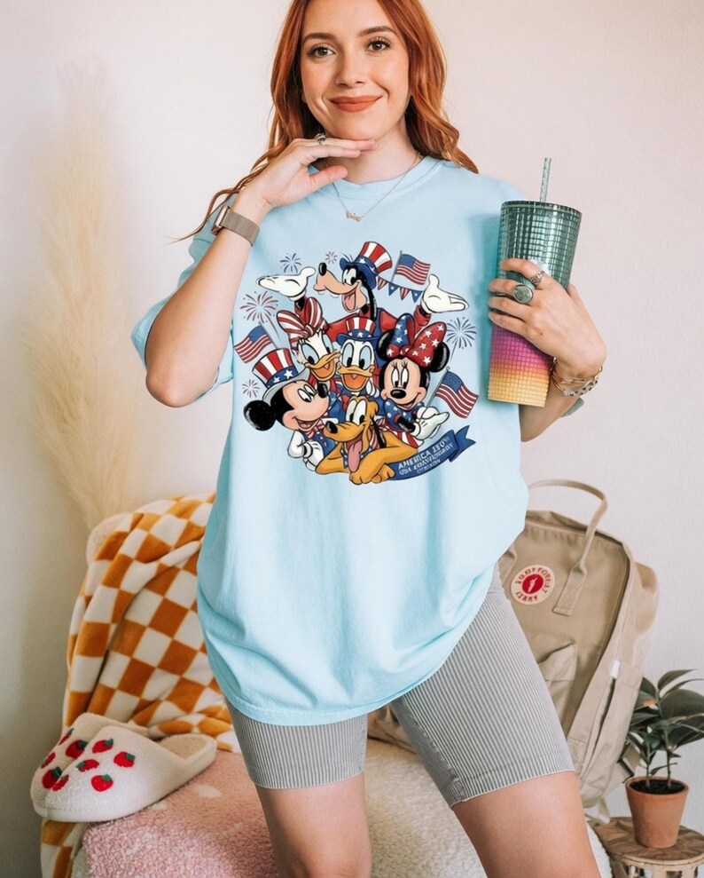 Mickey and Friends in patriotic hats with American flags and fireworks on a light blue t-shirt.