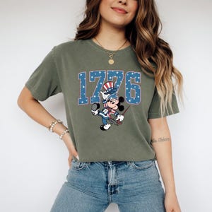 A woman wearing a green t-shirt with a graphic of a cartoon character and the number 1776 printed on it.