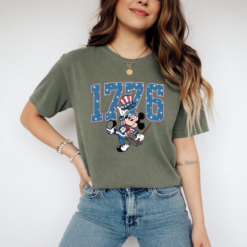 A woman wearing a green t-shirt with a graphic of a cartoon character and the number 1776 printed on it.