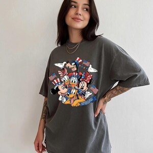 Mickey and Friends in patriotic hats with American flags, celebrating Independence Day 2026 on a t-shirt.