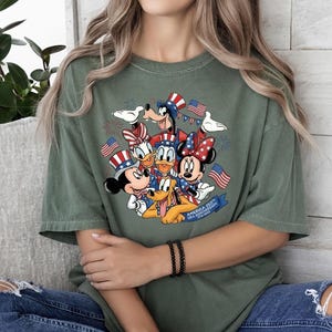 Mickey and Friends in patriotic hats with American flags and fireworks, celebrating USA 250th on a t-shirt.