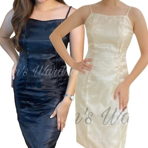 May include: Two sleeveless midi dresses with thin spaghetti straps and a square neckline. One dress is solid black and the other is solid cream. Both garments feature a vertical seam down the center of the bodice and a smooth, slightly lustrous fabric.