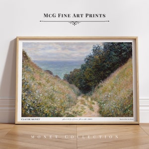 Puede incluir: Una impresión enmarcada de una pintura de Claude Monet titulada "Road to Le Caux, Pourville 1882". La pintura representa un camino que conduce a través de una ladera cubierta de hierba hacia el mar. El cielo está nublado y el agua es de un azul claro.