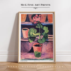 Puede incluir: Una impresión artística enmarcada titulada MCG Fine Art Prints que presenta una pintura de Henri Matisse de un geranio en maceta con flores rosas y hojas verdes en una maceta de terracota, sobre un fondo de superficies horizontales moradas y naranjas.