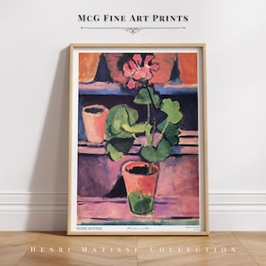 May include: A vintage art print of a still life painting by Henri Matisse featuring a pink geranium plant in a terracotta pot. The painting is set against a background of purple, blue, and orange hues. The print is framed in a light wood frame.