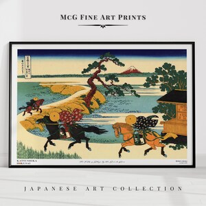 May include: Framed Japanese art print featuring a landscape with horses and riders. The artwork showcases a mountain in the background, a winding path, and a traditional building. The print includes text at the bottom and top of the image.