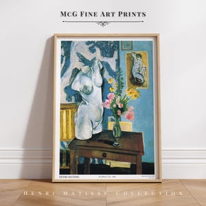 Puede incluir: Una pintura de Henri Matisse titulada "La Paleta, La Flor, El Desnudo" representa un busto de yeso blanco de una mujer, un jarrón de flores y un cuadro enmarcado de una mujer desnuda. La pintura está sobre un fondo azul con un papel tapiz estampado.