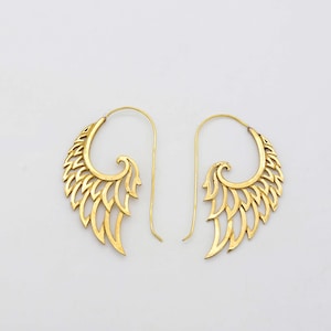 Op de afbeelding: Een paar goudkleurige oorbellen in een vleugelontwerp. De oorbellen hebben een gebogen bovenkant met een veervormig patroon en een lange, dunne haak voor doorboorde oren. De oorbellen worden tegen een witte achtergrond gepresenteerd.