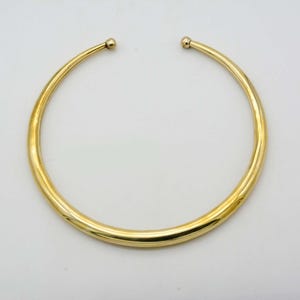 May include: A gold-toned choker necklace with a smooth, rounded surface.