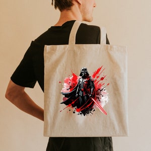 Op de afbeelding: Beige draagtas met een afbeelding van Darth Vader met een rood lichtzwaard. Het kunstwerk heeft een aquareleffect met rode en zwarte verfspatten. De tas heeft twee beige hengsels.