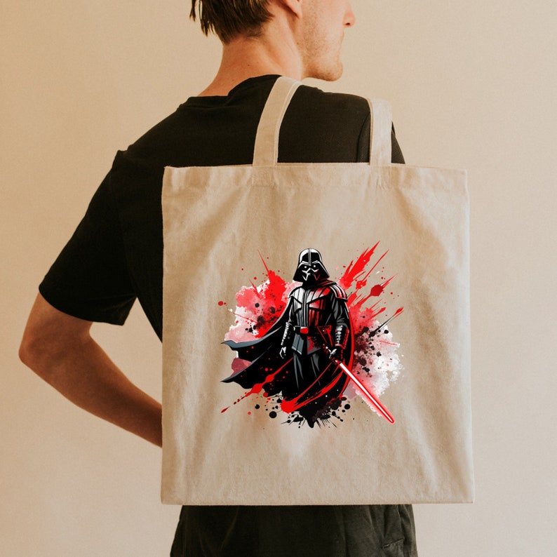Op de afbeelding: Beige draagtas met een afbeelding van Darth Vader met een rood lichtzwaard. Het kunstwerk heeft een aquareleffect met rode en zwarte verfspatten. De tas heeft twee beige hengsels.