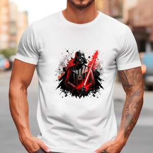 Op de afbeelding: Wit T-shirt met een afbeelding van Darth Vader met een rood lichtzwaard. Het ontwerp bevat zwarte en rode verfspatten. Het T-shirt heeft een ronde hals.