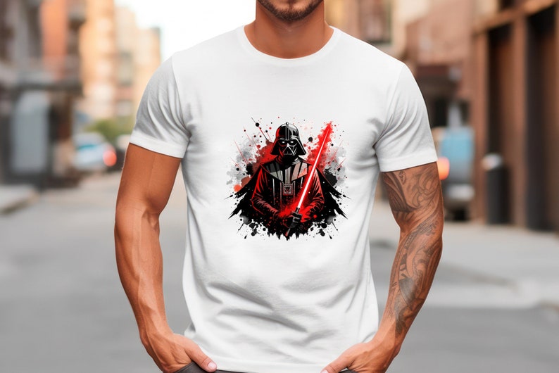 Op de afbeelding: Wit T-shirt met een afbeelding van Darth Vader met een rood lichtzwaard. Het ontwerp bevat zwarte en rode verfspatten. Het T-shirt heeft een ronde hals.