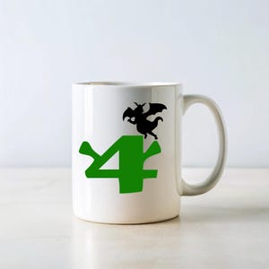 May include: White ceramic mug with a green number "4" and a black silhouette of a dragon on top. The dragon is facing right and has wings spread out.