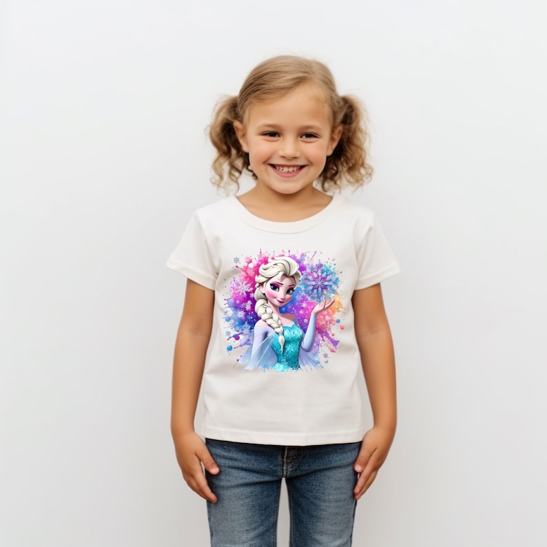 May include: White t-shirt with a colorful watercolor design featuring a cartoon image of Elsa from Frozen. Elsa is wearing a blue and silver dress and holding a snowflake.
