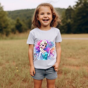 May include: A young girl wearing a white t-shirt with a colorful graphic of Elsa from Frozen. The graphic features Elsa holding a snowflake and is surrounded by colorful paint splatters.