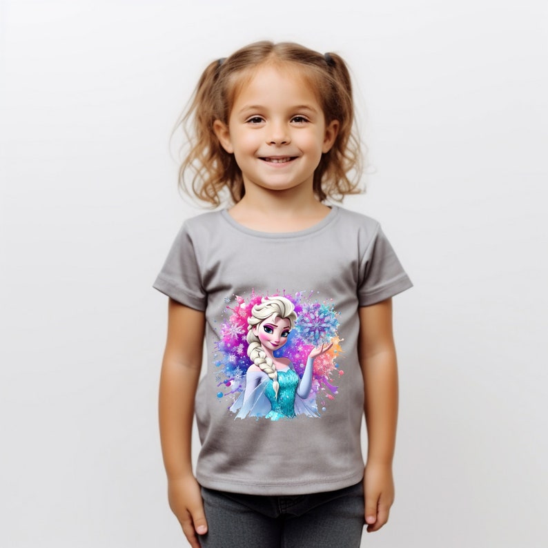 May include: A gray short-sleeved t-shirt with a colorful graphic print of Elsa from Frozen. The graphic features Elsa in her ice queen dress with a snowflake in her hand. The background is a watercolor-style design with blue, purple, and pink colors.