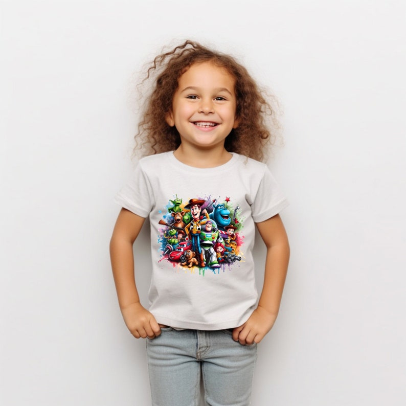 Op de afbeelding: Een wit T-shirt met een kleurrijke grafische print van personages uit de Toy Story-franchise. De personages zijn in een cirkelvormige opstelling geplaatst met een spattende kleurrijke verf erachter.