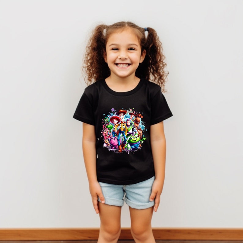 Op de afbeelding: Een zwart T-shirt met een kleurrijke grafische print van personages uit de Toy Story-filmfranchise. De personages zijn in een cirkel gerangschikt met een gespat effect.