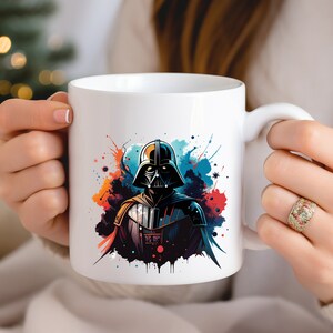 Op de afbeelding: Witte keramische mok met een gestileerde illustratie van Darth Vader, versierd met kleurrijke verfspatten. Het ontwerp bevat tinten zwart, blauw, rood en oranje. De mok heeft een standaard handvat.