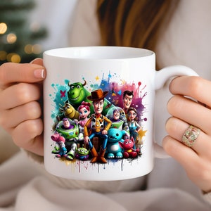 Op de afbeelding: Witte keramische mok met een kleurrijk aquarelontwerp met personages uit de Toy Story-franchise, waaronder Woody, Buzz Lightyear en Jessie. De personages zijn omringd door kleurrijke verfspatten.