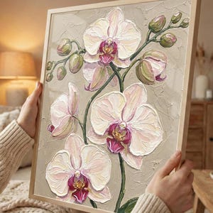 以下が含まれることがあります： 白とピンクの蘭の花の額装された絵画。テクスチャード加工されたインパストスタイル。詳細な花びらと緑の茎がニュートラルな背景に描かれています。フレームは明るい木の色で、花の主題を引き立てています。