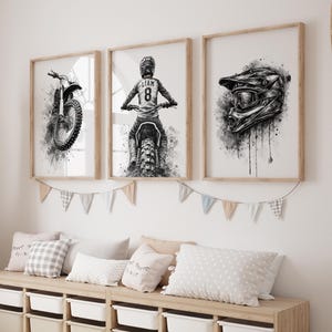 May include: Three framed monochrome motocross art prints. The prints show a motorbike, a rider with the name "Liam" and the number 8, and a helmet. The prints are displayed above a wooden bench with pillows.