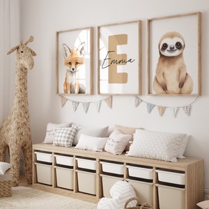 May include: Three framed prints with watercolor illustrations of a fox, a sloth, and the letter E with the name "Emma" written below. The prints are hanging on a white wall above a wooden shelf with storage bins.