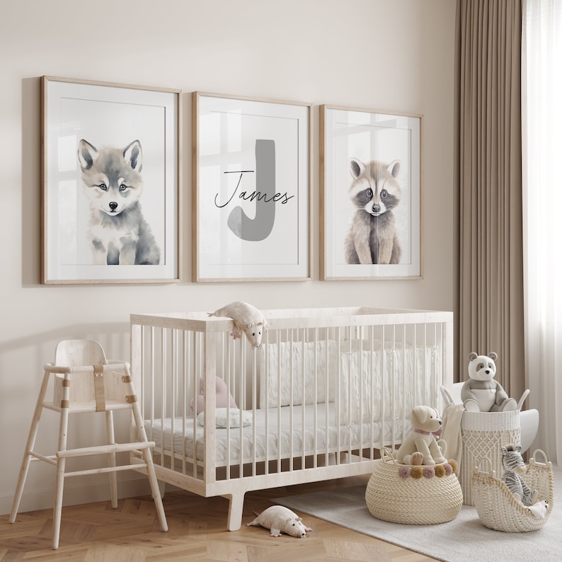May include: Three framed prints for a nursery, featuring a wolf, a raccoon, and a letter J with the name "James" written below. The prints are hung on a white wall above a white crib.