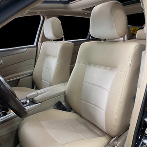 May include: Beige leather car seat covers with a white centre panel and a headrest. The seat covers have a quilted design and are installed in a car.