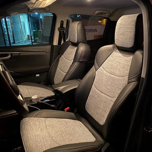 May include: Vehicle interior with two front seats. The seats are upholstered in black leather with gray fabric inserts. The headrests are also gray fabric. The interior is dark, with the word "TORNA" visible on a sign in the background.