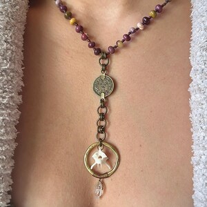 May include: A long necklace with a variety of small, colorful beads. The necklace has a pendant with a coin, a bone, and a crystal.