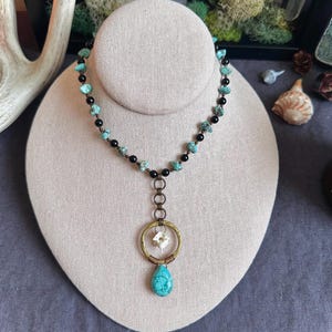 May include: A turquoise and black beaded necklace with a brass pendant featuring a turquoise stone and a bone charm.
