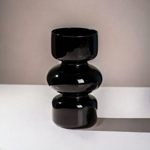 Peut inclure: Un vase en verre noir avec un design unique &agrave; trois niveaux arrondis. Le vase est fait de verre &eacute;pais et brillant et a une esth&eacute;tique moderne et minimaliste.