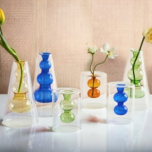 May include: A collection of colorful glass vases in various shapes and sizes. The vases feature shades of yellow, blue, orange, and green, with a clear outer layer. Some vases hold flowers, creating a vibrant display.