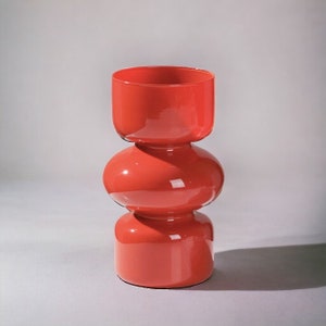 Peut inclure: Un vase en verre rouge et haut avec un design unique et bulbeux. Le vase est compos&eacute; de trois sections, chacune ayant une forme diff&eacute;rente. La section sup&eacute;rieure est un cylindre, la section m&eacute;diane est une sph&egrave;re et la section inf&eacute;rieure est un cylindre.