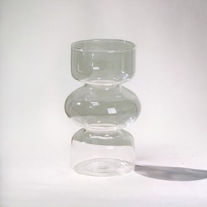 Peut inclure: Un vase en verre transparent avec un design unique &agrave; trois niveaux arrondis. Le vase est haut et fin, avec une large ouverture en haut.