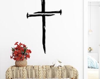 May include: A large, black metal cross made of nails is mounted on a white wall. Below, a bench with a woven, fringed cover holds a vase of red flowers and a white decorative object. The scene is brightly lit.