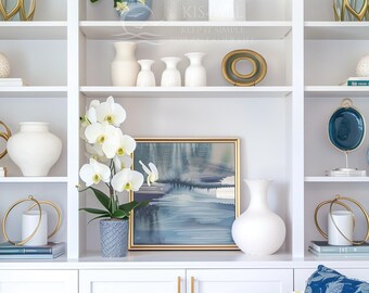 May include: White built-in shelving unit with various decorative items. Includes white vases, a framed landscape painting, gold-toned sculptures, potted plants, and a potted orchid with white flowers. The shelves are filled with home decor.