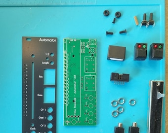May include: A green circuit board with the text "Timo Rozendal Automator v1.0" printed on it. The board is surrounded by various electronic components, including a black panel with the text "Automator" and "Timo Rozendal" printed on it, a black box, a black slider, and several black and green buttons.